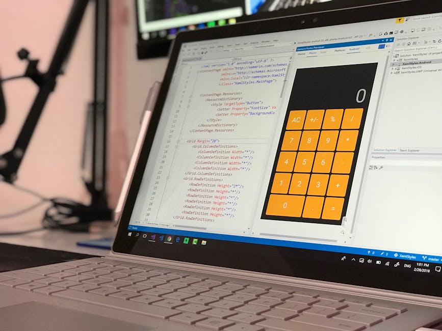 A person wearing a light blue shirt is seated at a desk working on a laptop, with their back to the camera. The laptop screen displays lines of colourful code on a dark background. To the right of the