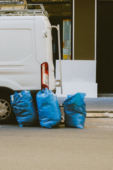 Three large blue plastic rubbish bags are placed on the pavement next to the rear of a white delivery van. The bags appear to be filled with waste materials, showing a somewhat wrinkled and bulky text